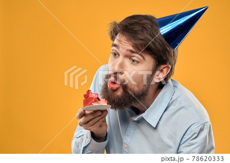 Man with cake on yellow background birthday party hat cropped view Man with cake on yellow background birthday party hat cropped view 78620333