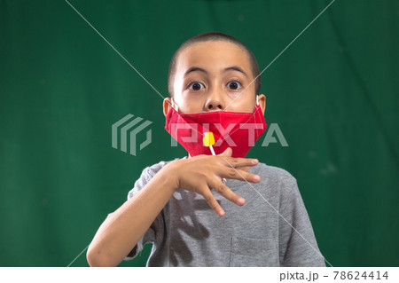 A cute caucasian young kid with red face mask. Protection versus viruses and infection.  Studio portrait, concept health with dark green background. 78624414