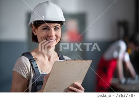 Portrait of woman worker with helmet indoors in factory holding clipboard. Portrait of woman worker with helmet indoors in factory holding clipboard. 78627787
