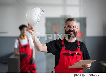 Portrait of cheerful worker with helmet and protective glasses indoors in factory looking at camera. Portrait of cheerful worker with helmet and protective glasses indoors in factory looking at camera. 78627788