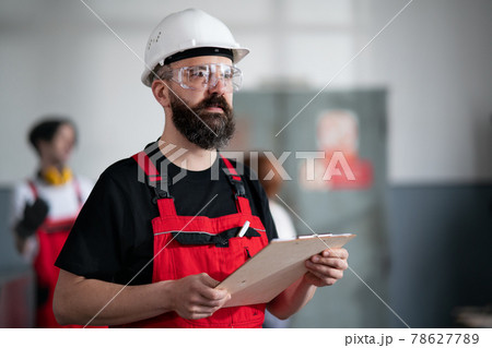 Portrait of worker with helmet and protective glasses indoors in factory holding clipboard. Portrait of worker with helmet and protective glasses indoors in factory holding clipboard. 78627789