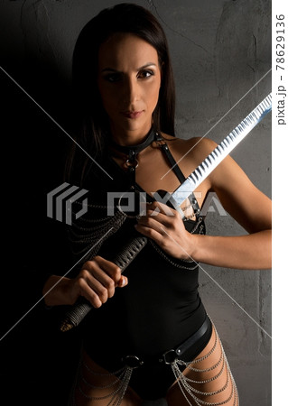 Woman in leather harness and with sword in studio Woman in leather harness and with sword in studio 78629136