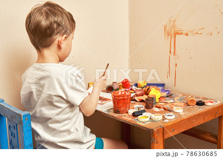 Little boy in t-shirt draws picture at messy table in room 78630685