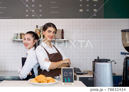 The shopkeeper and barista stand smiling with arms folded in front of a coffee shop counter. Morning atmosphere in a coffee shop. 78632434