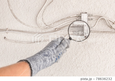 The hand of an industrial worker in a construction glove examines a large antenna splitter with a magnifying glass 78636232