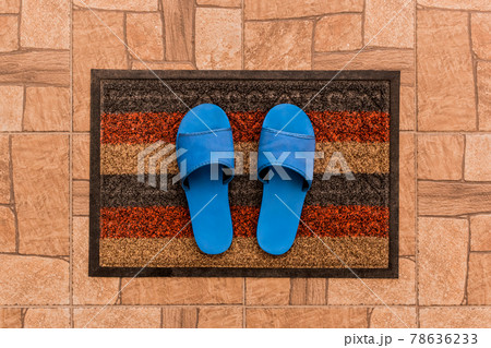 Men's blue house slippers stand on a foot mat on a brown tiled floor texture background, top view 78636233