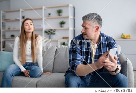 Mature woman feeling neglected because of her husband's smartphone overuse at home. Gadget addiction, phubbing Mature woman feeling neglected because of her husband's smartphone overuse at home. Gadget addiction, phubbing 78638782