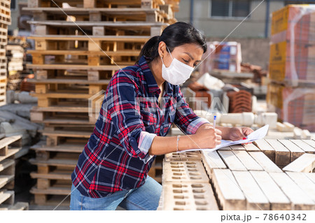 Woman in protective face mask controlling quantity of redbricks 78640342