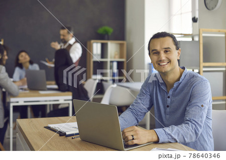 Portrait of happy young business man sitting at office desk with laptop computer 78640346