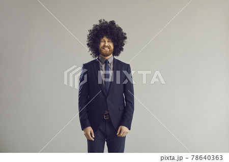 Happy businessman in elegant suit and crazy curly wig standing in studio and smiling Happy businessman in elegant suit and crazy curly wig standing in studio and smiling 78640363