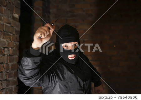 a bandit, terrorist, criminal in a black mask attacks with a knife in his hand in a dark room of an abandoned brick building a bandit, terrorist, criminal in a black mask attacks with a knife in his hand in a dark room of an abandoned brick building 78640800