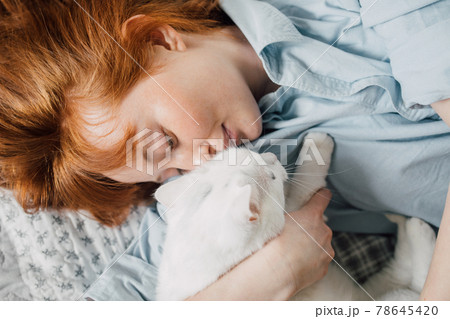 Woman embracing with her favourite white cat while laying at the bed 78645420
