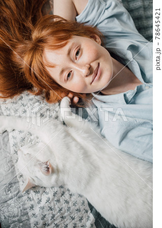 Woman looking at the camera and laying at the back at the bed near her white cat Woman looking at the camera and laying at the back at the bed near her white cat 78645421
