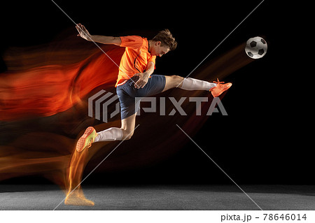 Young caucasian male football or soccer player kicking ball for the goal in mixed light on dark background. Concept of healthy lifestyle, professional sport, hobby. 78646014