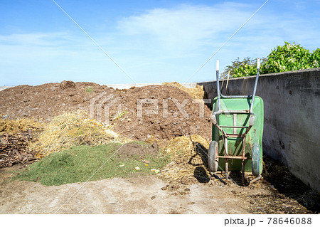 Green rusty wheelbarrow stands in a concrete container for crops, garbage or hay Green rusty wheelbarrow stands in a concrete container for crops, garbage or hay 78646088