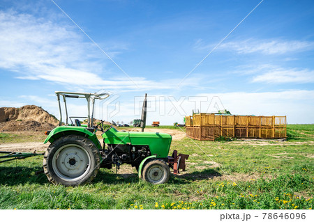 Green tractor stands on farm in field near agricultural fixtures at daytime Green tractor stands on farm in field near agricultural fixtures at daytime 78646096