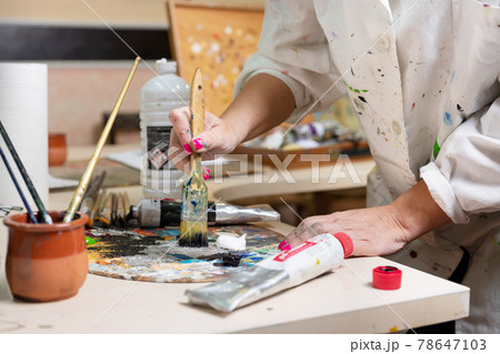 Creative female painter mixes palette of oil paints in palette. Close-up view 78647103