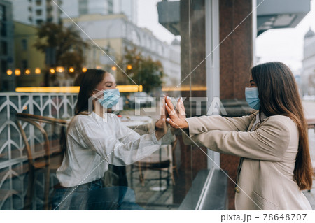 Two women in protective masks opposite each other, window between them. 78648707