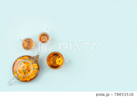 Cups of herbal tea, transparent teapot with calendula flowers on blue background. Calming drink concept. Copy space Flat lay Top view Cups of herbal tea, transparent teapot with calendula flowers on blue background. Calming drink concept. Copy space Flat lay Top view 78653516