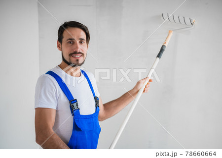 Smiling repairer stands near the wall and holds a roller in his hands Smiling repairer stands near the wall and holds a roller in his hands 78660664