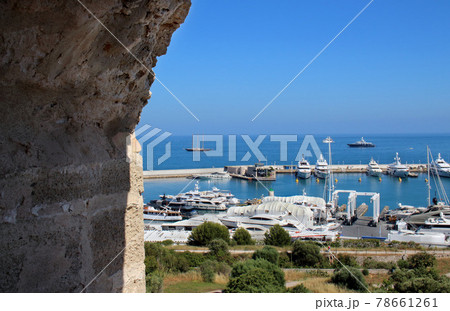 View on a port and yacht parking on blue sky and sea water background through big aged brick wall arched tower window 78661261