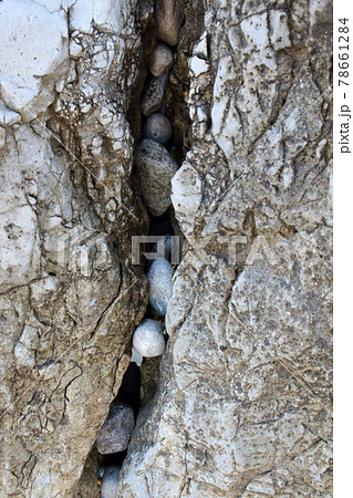 Small beach pebbles stones stuck in a crack between two big rocks vertical background 78661284