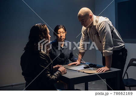 A police detective at the station and his partner, an asian woman, present evidence to a male suspect in an interview room. 78662169