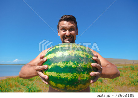 a man on the beach and holds a watermelon. ripening of summer berries Joyful emotions and mood. Summer picnic. a man on the beach and holds a watermelon. ripening of summer berries Joyful emotions and mood. Summer picnic. 78663189