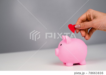 Faceless caucasian woman folds a small heart into a pink piggy bank on a white background. Love saving concept Faceless caucasian woman folds a small heart into a pink piggy bank on a white background. Love saving concept 78663836