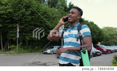 Young African-American man stands with an electric scooter and talks on a cell phone on the street. Ecological transportation. Urban outdoors. 78664698