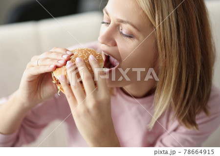 Young woman eating delicious appetizing hamburger at home 78664915