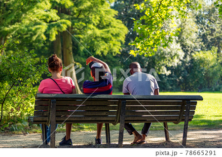 Three people sitting on a bench in the Amsterdam Vondelpark Three people sitting on a bench in the Amsterdam Vondelpark 78665291