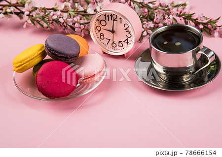 A cup of morning cappuccino with macaroons cookies and a pink alarm clock on a pink paper background. Copy space A cup of morning cappuccino with macaroons cookies and a pink alarm clock on a pink paper background. Copy space 78666154
