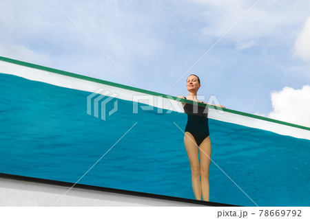 Young adult caucasian sporty slim smiling relaxing woman enjoy stand in pool with clear blue water and trasparent wall edge against sky at luxury spa resort. Healthy lifestyle and wellness concept Young adult caucasian sporty slim smiling relaxing woman enjoy stand in pool with clear blue water and trasparent wall edge against sky at luxury spa resort. Healthy lifestyle and wellness concept 78669792