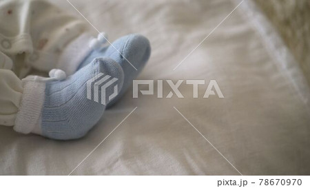 Newborn baby in blue socks. Tiny legs of the baby lie on a soft mattress, wear socks. Closeup of a young child in a home interior. Baby clothes concept Newborn baby in blue socks. Tiny legs of the baby lie on a soft mattress, wear socks. Closeup of a young child in a home interior. Baby clothes concept 78670970