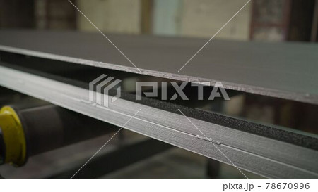 Continuous sheet of metallic material being fed through machine. Metal sheet on the conveyor. Painting large metal sheets in a factory Continuous sheet of metallic material being fed through machine. Metal sheet on the conveyor. Painting large metal sheets in a factory 78670996