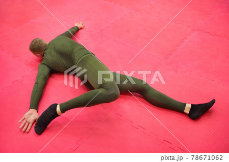 Young sports guy in a green thermal suit does exercises on the gym floor Young sports guy in a green thermal suit does exercises on the gym floor 78671062