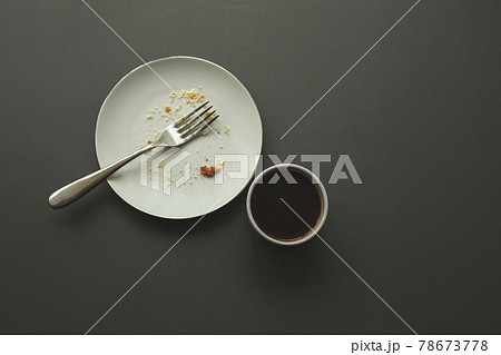 Empty plate with fork and crumbs and coffee cup after eating on gray background. Empty plate with fork and crumbs and coffee cup after eating on gray background. 78673778
