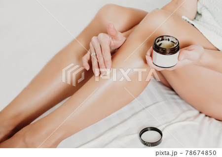 woman applying body butter on legs after shugaring procedure. depilation and after shave skin care concept 78674850