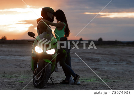 Couple embracing near motorbike on beach at sunset Couple embracing near motorbike on beach at sunset 78674933