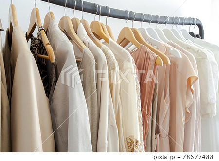 Stylish womans clothes hanging on a rack natural colors, trending concept,pastel colors in white room modern design closeup 78677488