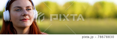 Happy young girl student listening music with headphones sitting outdoors in beautiful green park 78678830