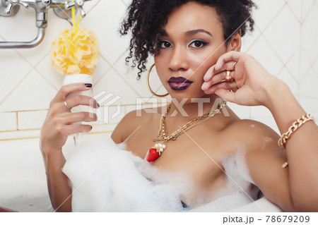 young afro-american teen girl laying in bath with foam, wearing swag jewelry flawless, making selfie 78679209