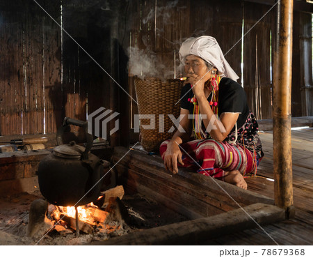 A portrait of karen tribe woman using cigarette to smoke, boiling water by using traditional kettle and fire, water heater at wooden kitchen at local home. People lifestyle. 78679368