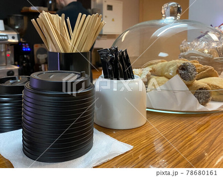 Natural wooden disposable sticks for mixing sugar in tea or coffee, sugar bowl, plastic thermo lids for cups and cakes on the bar in a small cafe Natural wooden disposable sticks for mixing sugar in tea or coffee, sugar bowl, plastic thermo lids for cups and cakes on the bar in a small cafe 78680161