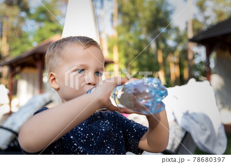 Portrait of cute playful little caucasian blond thirsty toddler boy kid holding plastic bottle and drinking water on hot summer day outdoors. Children heat dehydration danger awareness 78680397
