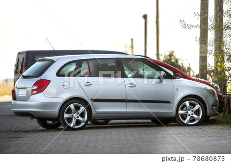 Side view of silver shiny luxurious car parked on empty paved road at low iron fence on background of small red mini vehicle and dark van on sunny day. Modern city lifestyle, parking problem concept. 78680873