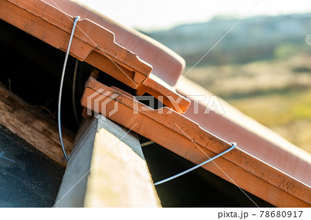 Closeup of metal montage anchor for installation of yellow ceramic roofing tiles mounted on wooden boards covering residential building roof under construction. Closeup of metal montage anchor for installation of yellow ceramic roofing tiles mounted on wooden boards covering residential building roof under construction. 78680917
