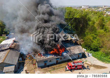 Aerial view of firefighters extinguishing ruined building on fire with collapsed roof and rising dark smoke. Aerial view of firefighters extinguishing ruined building on fire with collapsed roof and rising dark smoke. 78680988