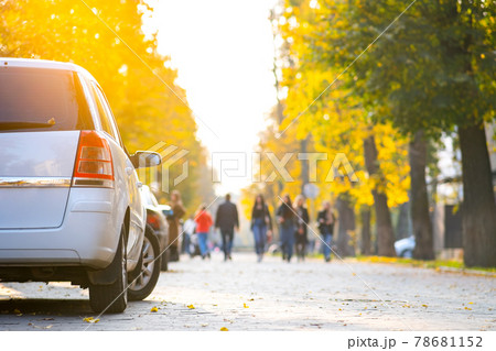 Cars parked in a row on a city street side on bright autumn day with blurred people walking on pedestrian zone. 78681152